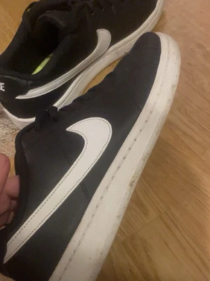 Svarta Nike sneakers med vit sula - Säljer ett par klassiska svarta Nike sneakers med vit sula och vit swoosh på sidan. Skorna har låg profil och är tillverkade i syntetmaterial med textilfoder. Perfekta för dig som gillar stilrena och sportiga skor. Skorna är i mycket bra skick knappt använda och har samt sko låda😊