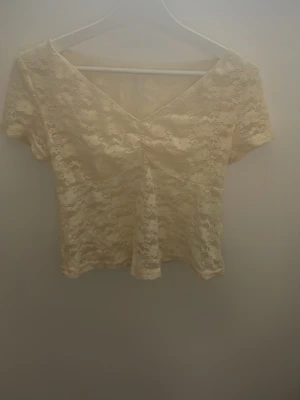 ljusgul spetsblus med v-ringning - Säljer en ljusgul blus med v-ringad hals och korta ärmar. Blusen är helt täckt av vacker spets med blommigt mönster och har en luftig känsla. Perfekt för dig som gillar romantiska detaljer och vill ha något lätt och snyggt.