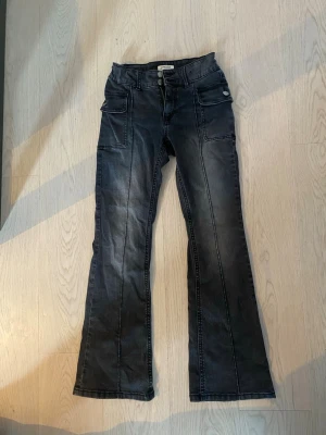 Y2k jeans - Säljer ett par svart/gråa Y2k bootcut jeans. ger en grunge vibe och är jättecoola, jeansen har inga fickor bak med istället på sidorna, är även justerbara i midjan så du kan anpassa dom efter hur du vill, sååå snygga!! 💕💕storlek 158/xxs/32