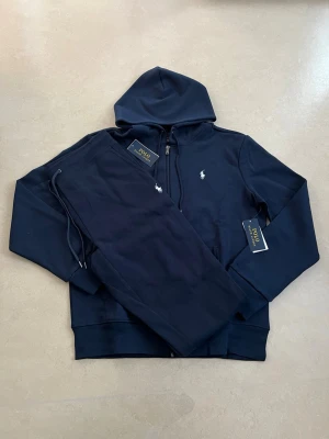 Ralph lauren tracksuit mörkblå storlek medium - Helt ny Ralph Lauren tracksuit (hoodie + byxor). En av de mest efterfrågade seten – perfekt för vardag och resor.  • Oanvänd / nyskick • Säljs som komplett set • Väldigt populär modell • Bekväm och stilren passform • Perfekt året runt  Storlek: M Färg: mörkblå  Skickas snabbt 📦 Rabatt vid köp av flera plagg.