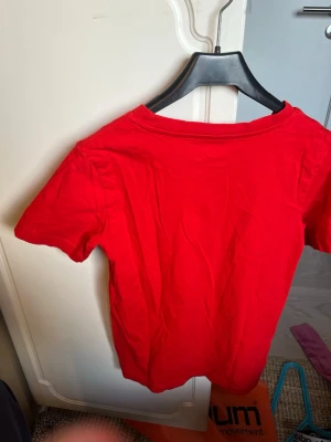 Röd t-shirt från C i storlek XS - En enkel och klassisk röd t-shirt från C i storlek XS. T-shirten har rund halsringning och korta ärmar. Perfekt basplagg att matcha med jeans eller kjol. Tillverkad i mjukt bomullsmaterial för skön känsla hela dagen.