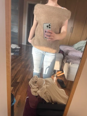 Beige stickad topp i mohairmix - Säljer en beige stickad topp med korta ärmar och bred halsringning. Tröjan är gjord i en mjuk mohairmix som ger en fluffig och lyxig känsla. Perfekt att styla med jeans eller kjol för en trendig look.