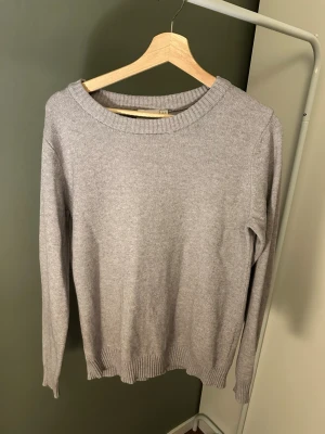 Ljusgrå stickad tröja i bomull - En enkel och stilren ljusgrå stickad tröja med rund halsringning och ribbade muddar vid ärmslut och nederkant. Perfekt basplagg i garderoben, tillverkad i mjuk bomull för skön känsla. Passar till det mesta och är lätt att matcha.