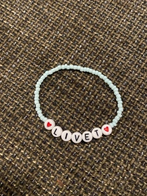 Pärlarmband med texten LIVET - Sött armband med ljusblå små pärlor och vita bokstavspärlor som stavar 'LIVET', samt två pärlor med röda hjärtan. Perfekt accessoar för dig som gillar personliga smycken och vill bära ett positivt budskap.