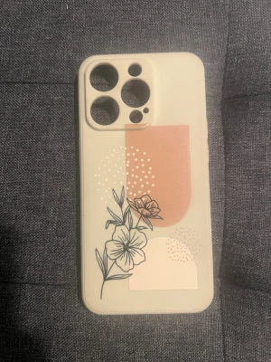 Beige mobilskal med blommor och mönster - Snyggt beige mobilskal med grafiskt mönster i rosa och vitt samt svart blommotiv. Skalets design har en modern känsla med stilrena linjer och prickar. Tillverkat i mjukt plastmaterial som skyddar mobilen och ger ett unikt uttryck.