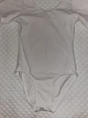 Vit leotard från Sansha - Vit leotard från Sansha med rund halsringning och korta ärmar. Tillverkad i ett stretchigt och mjukt material som ger bra rörelsefrihet, perfekt för träning eller dans. Det står strl 16år men jag skulle rekommendera denna till någon som är kankse 150/155. Den har lite färgfläckar men den är köpt på vinted så jag vet inte vad de kommer ifrån