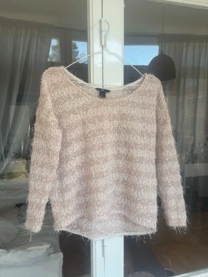 Ljusrosa fluffig stickad tröja - Mysig ljusrosa stickad tröja med fluffig textur och rund halsringning. Tröjan har långa ärmar och är tillverkad i ett mjukt, luddigt material som ger en avslappnad och trendig look. Perfekt för att hålla värmen under kyliga dagar.