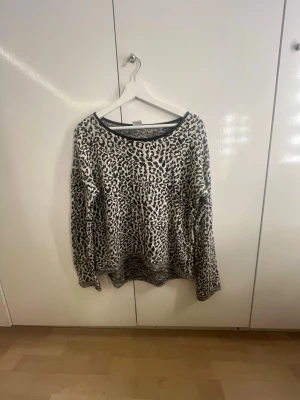 Leopardmönstrad stickad tröja - Säljer en snygg stickad tröja med leopardmönster i svart och vitt. Tröjan har rund halsringning, långa ärmar och ribbstickad kant nedtill. Perfekt för dig som vill ha en trendig och bekväm look till hösten eller vintern.
