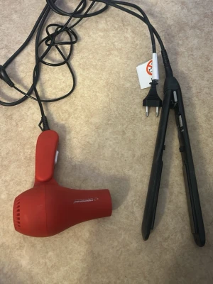 Hårfön och plattång elektronikpaket - Säljer ett paket med en röd hårfön  och en svart plattång. Hårfönen har kompakt design och sladd med EU-kontakt. Plattången är svart och smal, perfekt för styling av håret. Båda är elektriska och enkla att använda.