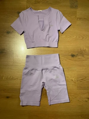 Ljuslila träningstopp och cykelbyxor ICANIWILL - Säljer ett ljuslila ribbat träningsset från ICANIWILL med kortärmad topp och matchande cykelbyxor med hög midja. Setet är gjort i stretchigt material och har diskret logga på både topp och byxor. Perfekt för gym eller hemmaträning.