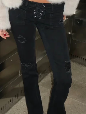 Svarta lace-up jeans med slitningar - Snygga svarta jeans med lace-up-detalj i midjan och slitningar på låren och knäna. Jeansen har en rak passform med bootcut. Helt oanvända. Storlek S 