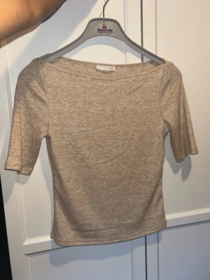 Zara 3/4 topp - En enkel och stilren beige topp med korta ärmar. Toppen har en bred, något båtformad ringning och är lätt croppad. Perfekt att matcha med både jeans och kjol.