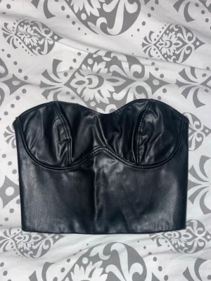 Svart korsettopp i skinnimitation - Snygg svart korsett-topp i skinnimitation med bygel och formade kupor. 