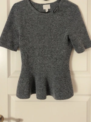 Grå ribbad topp från H&M - Superfin grå ribbad topp från H&M med korta ärmar och lätt utsvängd nederdel. Mjuk stickad känsla och rund halsringning, perfekt för lager-på-lager eller som den är. Enkel att styla till både jeans och kjol. Den är använd 1-2 gånger men som ny, säljer då den inte kommer till användning. Storlek S