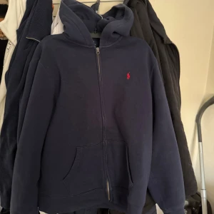 Mörkblå zip hoodie från Polo Ralph Lauren - Mörkblå hoodie med dragkedja från Polo Ralph Lauren. Inte använd mycket så har mest varit i garderoben. Äkta. Storlek 18-20 (xl) men skulle säga att den är liten i storlek för jag har medium på kläder och den sitter bra