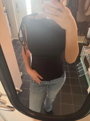 Svart snörad topp från Gina Tricot - Snygg svart topp från Gina Tricot i figurnära modell. Toppen har snörning på ena axeln och är ärmlös, vilket ger en trendig look. Perfekt att styla med jeans eller kjol för en cool outfit.