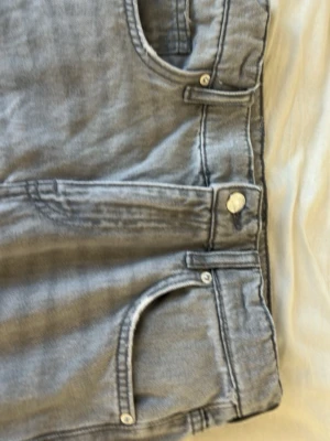 Grå jeans från Zara - Säljer ett par grå jeans från Zara med klassisk femficksdesign och silverfärgade knappar. Jeansen har bälteshällor och är tillverkade i ett mjukt denimtyg som passar perfekt till en avslappnad stil.
