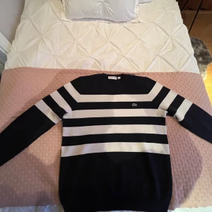 Snygg Lacoste-tröja – marinblå & vit, Mycket bra skick - Stilren randig Lacoste-tröja i marinblått och vitt. Klassisk modell med det broderade krokodilmärket på bröstet. Mjuk, bekväm och i fint skick. Perfekt för både vardag och mer dressade outfits