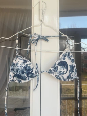 Blåvit blommig trekantsbikini - Snygg trekantsbikini i blått och vitt med blommigt mönster. Klassisk modell med knyt i nacken och ryggen, perfekt för sommardagar på stranden. Materialet känns mjukt och följsamt mot huden.