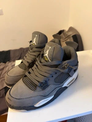 Gråa Air Jordan 4 Retro sneakers Cool Grey - Snygga Air Jordan 4 Retro sneakers i grått med svarta och vita detaljer. Skorna har meshpaneler, klassisk Jumpman-logga på plösen och robust sula med synlig Air-enhet. Ovandelen är i mocka och läder, perfekt för dig som gillar streetwear och basketstil.