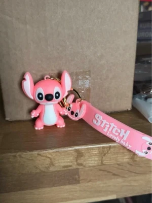 Rosa Stitch nyckelring med band - Söt rosa Stitch-figur som nyckelring med matchande band där det står 'Stitch Lovely Baby'. Perfekt accessoar till väskan eller nycklarna för dig som gillar Disney och kawaii-stil.