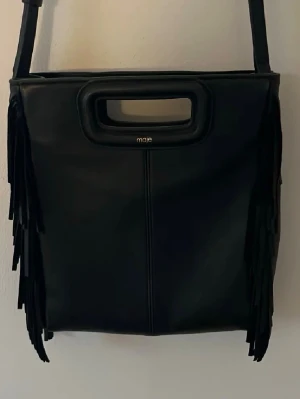 Svart handväska Maje - Supersnygg svart maje väska i läder med fransar på sidorna. Väskan är köpt på NK och är i nytt skick då den inte är så använd!