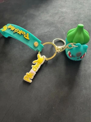 Pokémon Bulbasaur Nyckelring - Cool grön nyckelring med Pokémon-logga i gult och blått, tillverkat i plast. Perfekt som accessoar för Pokémon-fans som vill sticka ut och visa sitt intresse. Nyckelringen har en lekfull design och är lätt att bära.