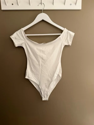 Vit basic body med kort ärm - Enkel och stilren vit body med korta ärmar och bred urringning. Tillverkad i mjukt och stretchigt material som sitter skönt mot kroppen. Perfekt att matcha med jeans eller kjol för en clean look.