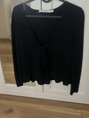 Svart knytblus från Ivyrevel - Stilren svart blus från Ivyrevel med v-ringning och knyt framtill. Långärmad modell med lätt vågig nederkant som ger en snygg touch. Perfekt att matcha med både jeans och kjol.