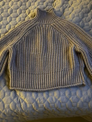 Grå ribbstickad polotröja - Säljer en grå ribbstickad polotröja med hög krage och långa ärmar. Tröjan har en chunky stickning och är gjord i ett mjukt garn, perfekt för kyliga dagar. Passar dig som gillar en avslappnad men ändå trendig look.