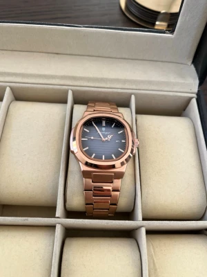 Ekstrand PP Roséguld/Blå - Stilren herrklocka i roséguld med blå urtavla. Klockan har länkarmband i metall, datumvisning och tydliga indexmarkeringar. Perfekt accessoar för dig som vill ha en modern och elegant look.