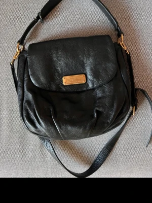 Marc Jacobs väska  - Säljer denna fina och tidlösa väska i läder från Marc Jacobs. Generellt superfint skick både på insidan och utsidan. Tyvärr lite slitage på ena sidan av axelremmen (se bild). Ett axelband samt ett längre justerbart och avtagbart band.  Ett innerfack med dragkedja och två små öppna innerfack.   Inköpt på Raglady.