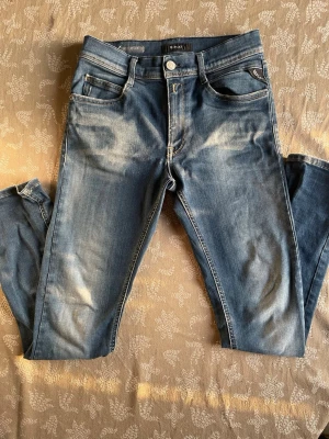 Blå slim fit jeans från Replay - Säljer ett par blå slim fit jeans från Only & Sons med snygga slitningar och klassisk femficksmodell. Jeansen har normal midja, dragkedjegylf och är tillverkade i mjuk denim med 