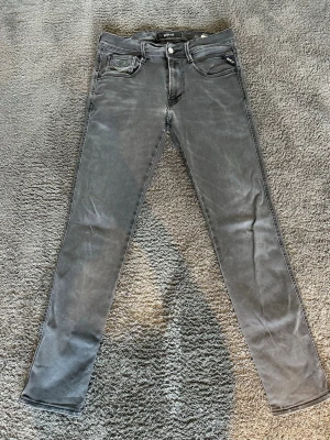 Replay jeans - Säljer ett par gråa slim fit jeans från Replay med klassisk femficksdesign och snygga detaljer på bakfickorna. Jeansen har en knappstängning och är tillverkade i ett stretchigt material som ger en skön passform.