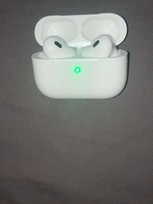 Apple AirPods Pro med laddningsetui - Säljer ett par vita Apple AirPods Pro med tillhörande laddningsetui. Hörlurarna är in-ear och har en stilren, kompakt design med touchfunktioner. Etuiet är gjort av plast och har LED-indikator för batteristatus. Perfekt för trådlös musik och samtal.
