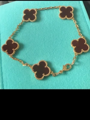 Van Cleef Roseguld Röd - Snyggt armband med guldfärgad kedja och mörka pärlor i klöverform. Pärlorna är infattade i guldfärgade kanter som ger ett exklusivt intryck. Perfekt för dig som vill ha en elegant och trendig accessoar.