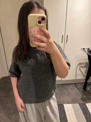 Mörkgrå stickad tröja med kort ärm - En enkel och stilren mörkgrå stickad tröja med korta ärmar och rund hals. Tröjan har en rak passform och är gjord i ett mjukt stickat. Strl 158/164 och från Gina tricot.