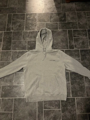 Grå hoodie från Samsøe Samsøe - Snygg ljusgrå hoodie från Samsøe Samsøe med minimalistisk logga på bröstet. Klassisk känguruficka framtill, justerbar huva med dragsko och ribbade muddar. Perfekt för en chill och avslappnad stil. Tillverkad i mjukt sweatshirtmaterial. Inge defekter använts 2 gånger max, säljer då den är för stor på mig