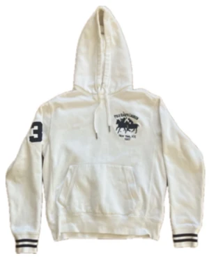 Vit hoodie från Polo Ralph Lauren - Vit hoodie från Polo Ralph Lauren med stor huva och känguruficka. Tryck med logga och text på bröstet samt en stor siffra 3 på ena ärmen. Ribbstickade muddar med svarta ränder. Klassisk och sportig look, perfekt till jeans eller joggers. OBS. Tveka inte på att höra av er vid frågor!