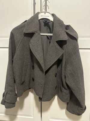 Grå Kappa från hm - Stilren grå kort rock med bred krage och dubbelknäppning. Perfekt för kyliga dagar. Storlek S men den passar mer M/ L 