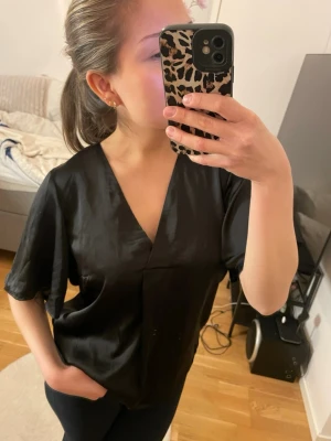 Svart v-ringad blus i satin - Snygg svart blus i glansigt satinmaterial med v-ringning och avslappnad passform. I storlek S från Bubbleroom💕