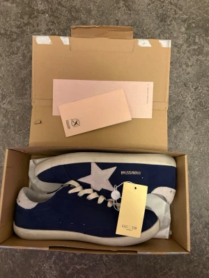 Blå Golden Goose sneakers med stjärna - Snygga blå sneakers från Golden Goose med vit stjärndetalj på sidan och vita suffletter. Skorna har vita snören och en klassisk låg siluett. 