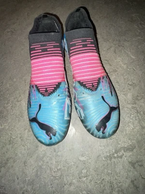 Puma blå och rosa fotbollsskor - Säljer ett par grymma fotbollsskor från Puma i blått och rosa med svarta detaljer. Skorna har en strumpliknande design utan snörning och är tillverkade i syntetmaterial för bästa passform och bollkontroll. Perfekta för dig som vill sticka ut på planen!