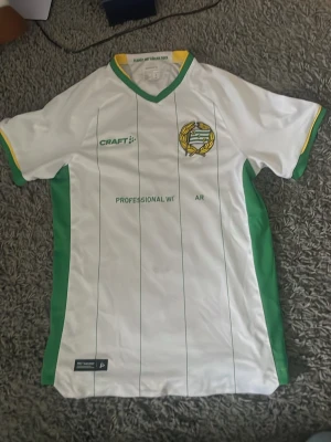 Vit fotbollströja Hammarby Craft - Snygg vit fotbollströja från Craft med Hammarby IF:s klubbmärke på bröstet. Tröjan har gröna och gula detaljer, smala gröna ränder och gröna sidopaneler. Tillverkad i ett lätt och funktionellt material som andas, perfekt för träning eller match. Några av bokstäverna har låsnat och Bajen loggan har flyttats ner lite lite som ni ser på bilden. Annars är den i fint skick.