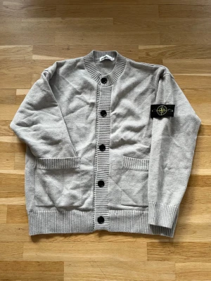 Grå cardigan från Stone Island - En superunik tröja! Knappt anvand, i nyskick. Tröjan ar tjock, varm och perfekt för våren, både för en fin och bekväm look. Tröjan ar för män. Den är i storlek M men passar mer som L. Passar dig som ar ungefar 175-190 cm lång och väger 75-90kg. Hör gärna av dig om du har några frågor eller funderingar!