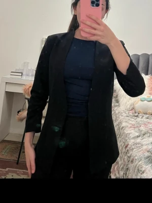 Svart klassisk kavaj - Snygg svart kavaj med enkel, rak passform och smala slag. Kavajen har långa ärmar och är tillverkad i ett slätt tyg som ger en stilren look. Perfekt att matcha med både jeans och kostymbyxor för en clean outfit.