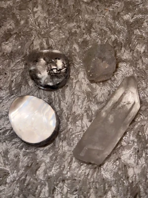 Samling av fyra olika kristaller - Fyra olika kristaller och stenar: en klar kvartsstav, en rund vit pärlemorsten, en svartvit dendritisk agat och en rå, ljusgrå kristall. Perfekt för dig som gillar kristaller, dekoration eller samling.