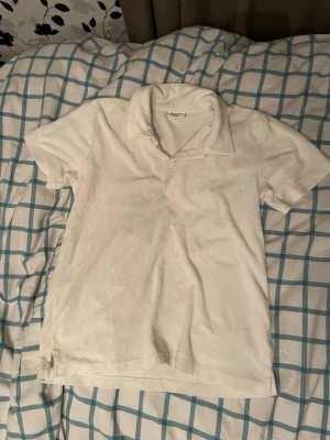 Vit frottéskjorta från Kappahl - Vit skjorta från Kappahl i mjuk frotté med klassisk krage och korta ärmar. Perfekt för en avslappnad och chill stil. Enkel design utan mönster eller detaljer, vilket gör den lätt att matcha med allt.