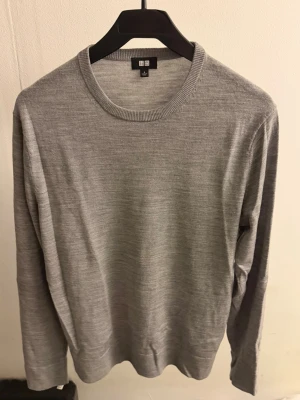Grå stickad merinoull tröja från Uniqlo - Snygg och enkel grå stickad tröja från Uniqlo med rund halsringning och långa ärmar. Tillverkad i tunt, mjukt material (merinoull) som sitter slimmat på kroppen. Perfekt basplagg för lager på lager och passar till det mesta.