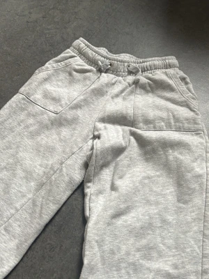 Grå mjukisbyxor med dragsko - Säljer ett par klassiska grå mjukisbyxor med resår i midjan och dragsko. Byxorna har två stora fickor framtill och är gjorda i mjukt sweatshirtmaterial. Perfekta för chill dagar eller när du vill vara extra bekväm.